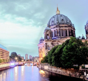 Berliner Dom bei Abendd&auml;mmerung mit Blick auf die Spree und die beleuchtete Stadt im Hintergrund.