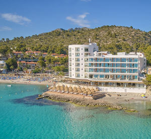 Modernes Strandhotel mit direktem Zugang zum türkisblauen Meer und Sonnenschirmen am Sandstrand.