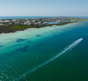 Luftaufnahme der Küste von Florida mit türkisfarbenem Wasser, einem Motorboot mit weißer Spur und Häusern entlang des Strandes.