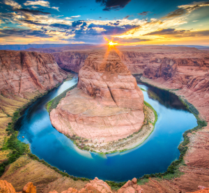 Hufeisenförmige Flussschleife zwischen roten Canyonwänden bei Sonnenuntergang.