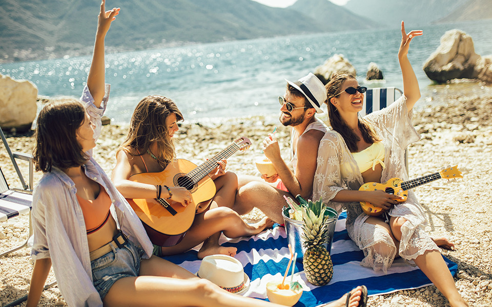 Super Last Minute Urlaub: Freunde am Strand spielen Gitarre