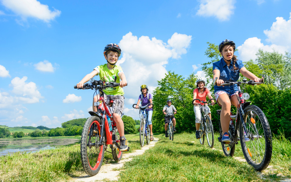 Familie und Kinder fahren mit dem Fahrrad entlang eines Weges am Gardasee bei sch&ouml;nem Wetter.
